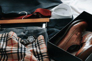 A styled Burberry outfit laying on the bed. Ensemble includes a suit, scarf, shoes and tie, all burberry along with a watch which is not Burberry.