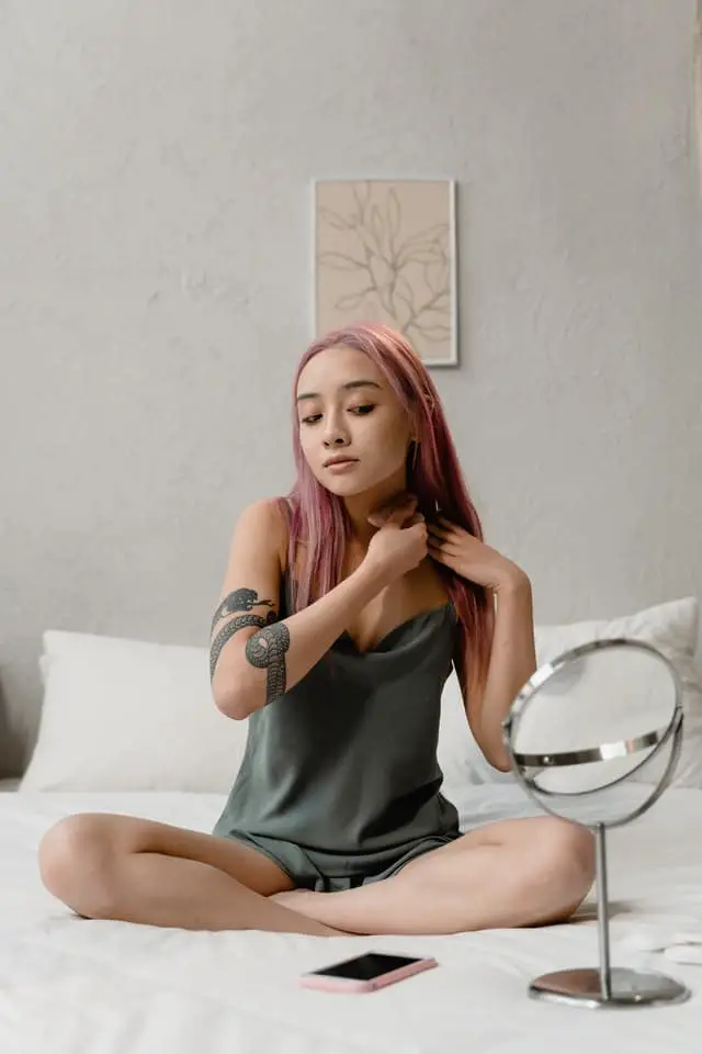 Girl with pink hair and green pajamas looks in the mirror on her bed in her bedroom