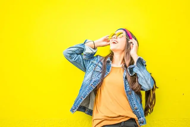 Girl in a denim jacket and mustard yellow top with sunglasses on yellow background