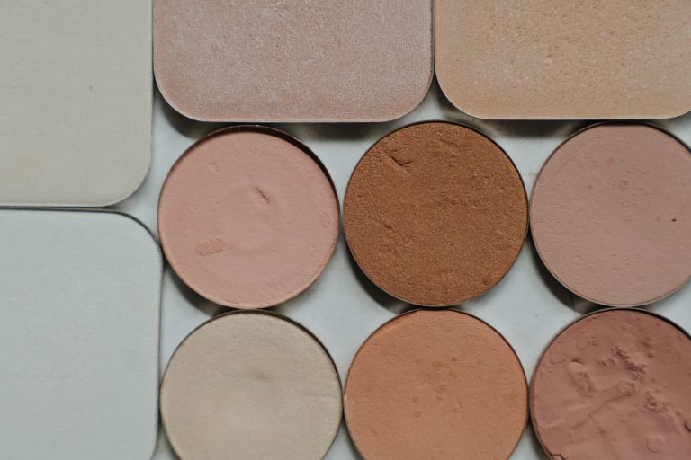 Powdered make-up in varying neutral shades of brown, gold, rust, and grey in round and square containers.