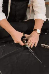 a man with fabric scissors wearing a watch and cutting black fabric laid out on a table